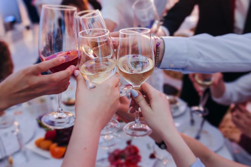 Group of guests celebrate and raise glasses, toasting and cheering with alcohol glasses with wine and champagne in a restaurant on corporate christmas, birthday party prom event or wedding celebration