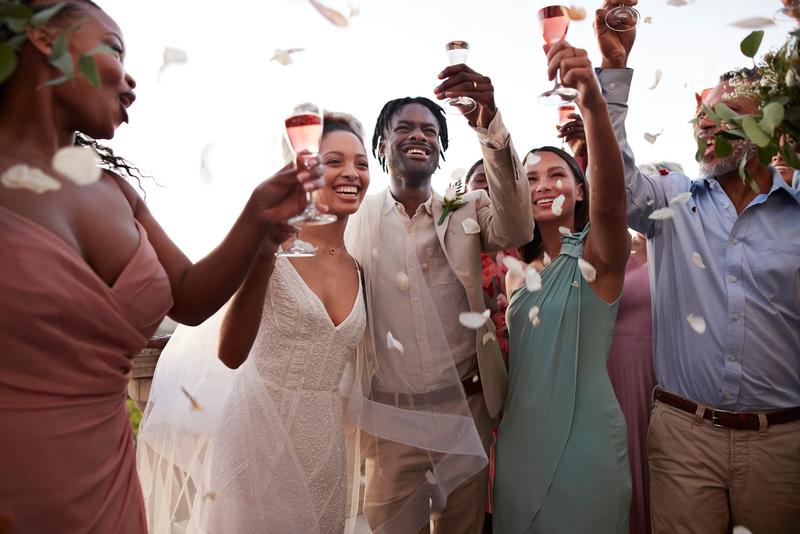 Confetti falling on cheerful just married couple and guests during wedding reception at sunset