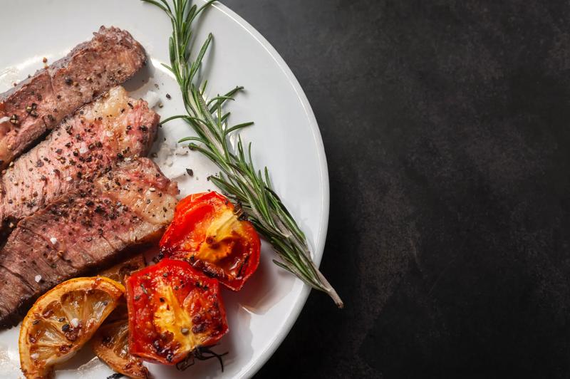 Sliced grilled wagyu steak served on white plate with grilled sliced lemon, tomatoes, garlic and rosemary.