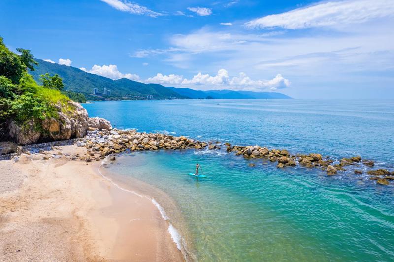 A large sprawling ocean and beach, a paddle boarder can be seen from afar