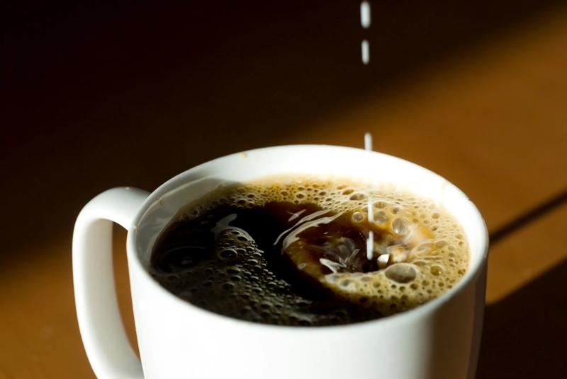 Creamy half and half drips into a large ceramic cup of black coffee, causing large bubbles and a splash.