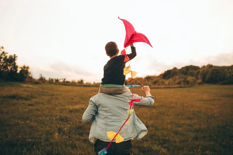 Little boy is running a kite with his father, on a beautiful day they are spending outdoors in nature
