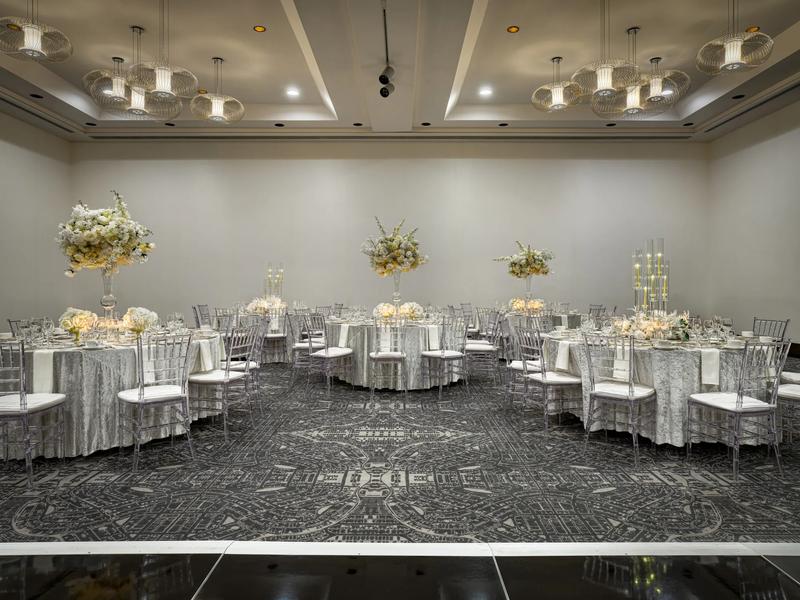 A reception for a wedding decorated with white table clothes, three floral center pieces and two candle center pieces